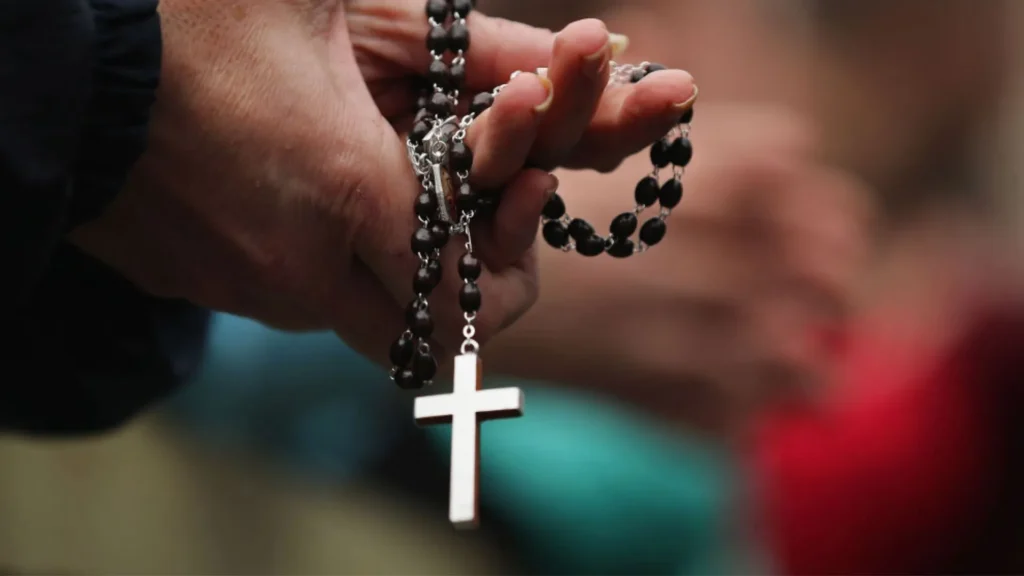 Close-up of a person's hands holding a rosary with a cross, focusing on prayer beads