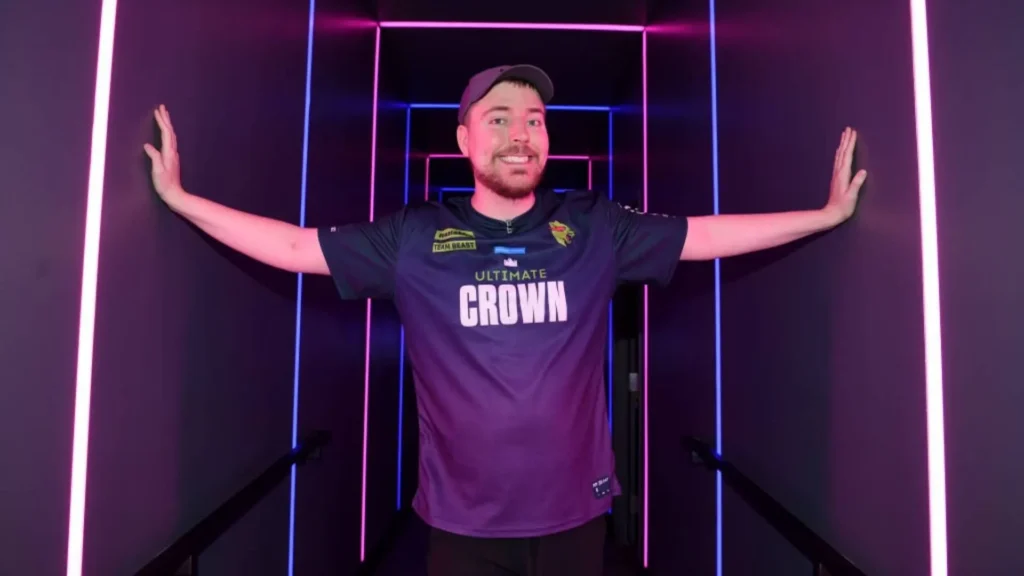 MrBeast in a vibrant gaming room with purple lighting, wearing a team jersey and extending his arms with a smile
